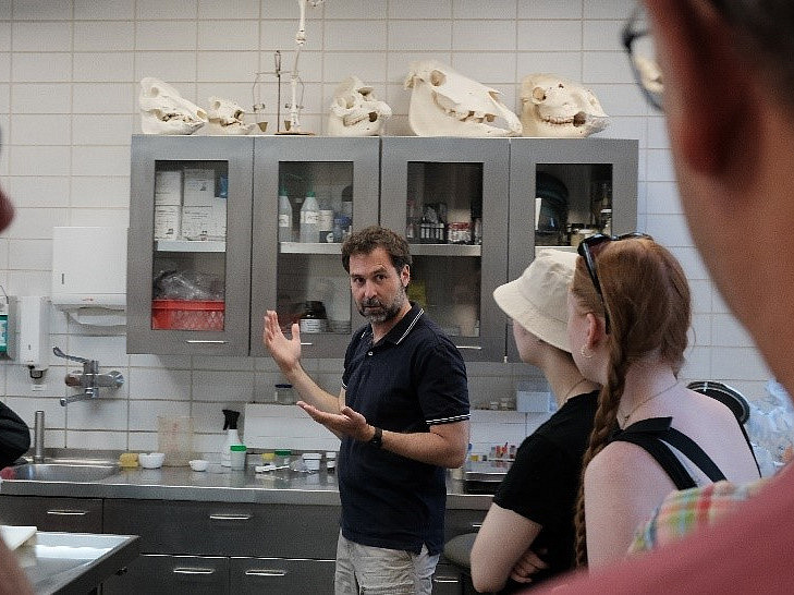 Chadi Touma stands in front of students in a laboratory and appears to be explaining something. Animal skulls can be seen in the background.