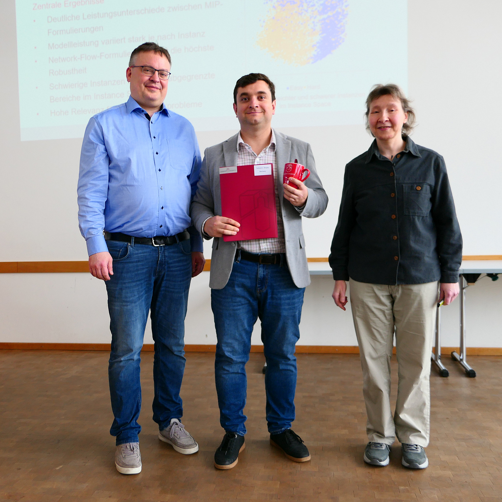 Ein Student steht mit seinem Abschlusszeugnis zwischen Dekan und Studiendekanin.