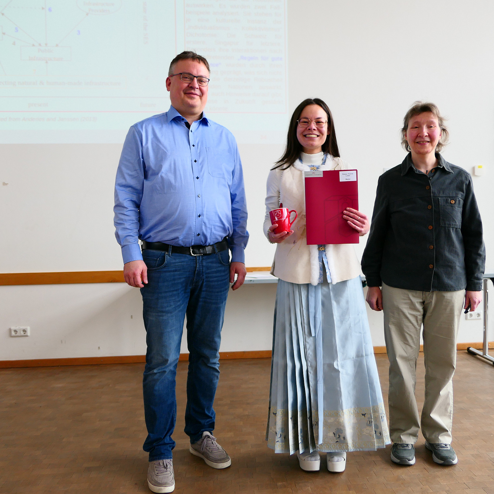 Eine Studentin steht mit ihrem Abschlusszeugnis zwischen Dekan und Studiendekanin.