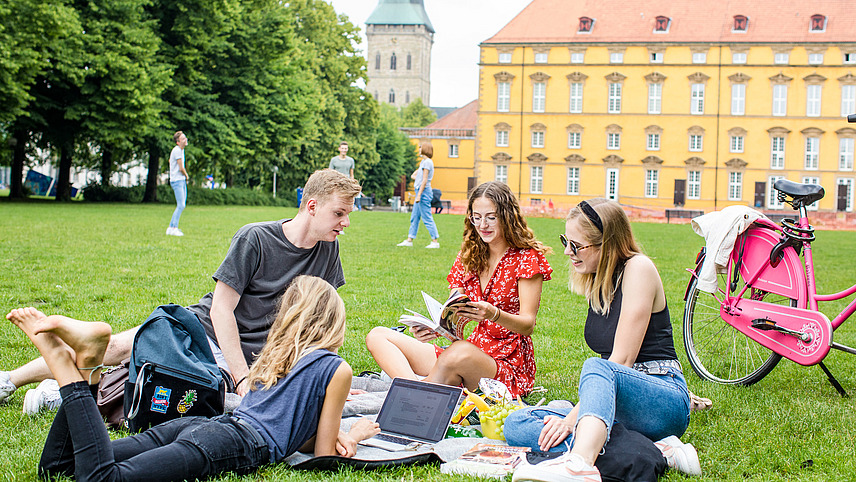 Vier Studierende sitzen auf einer Decke im Schlossgarten. Neben ihnen steht ein pinkes Fahrrad.