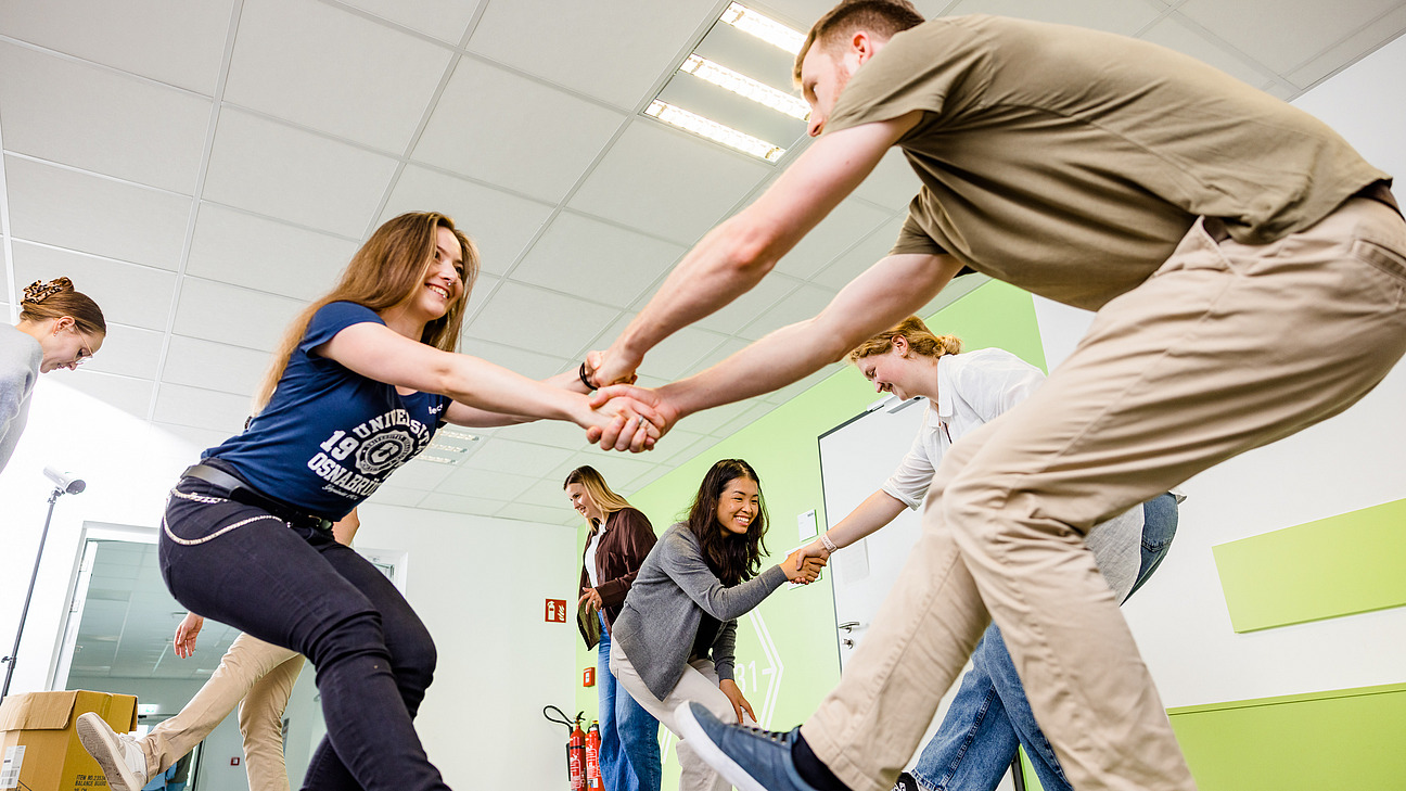 Zwei Studierende halten sich an den H&auml;nden, und f&uuml;hren eine Bewegungs&uuml;bung im Rahmen einer bewegten Pause durch.