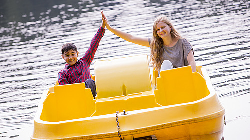 A child and a woman sit on a pedal-boat doing a high five.