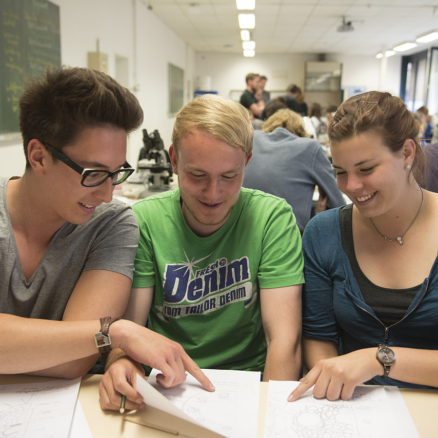 Drei Studierende sitzen an einem Tisch und diskutieren.
