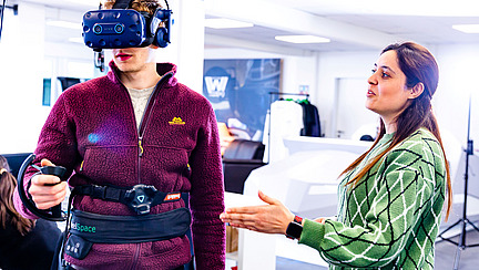 Im VR-Lab erklärt eine Studentin einem Probanden, der die VR-Brille anhat, was er beim Experiment machen soll.