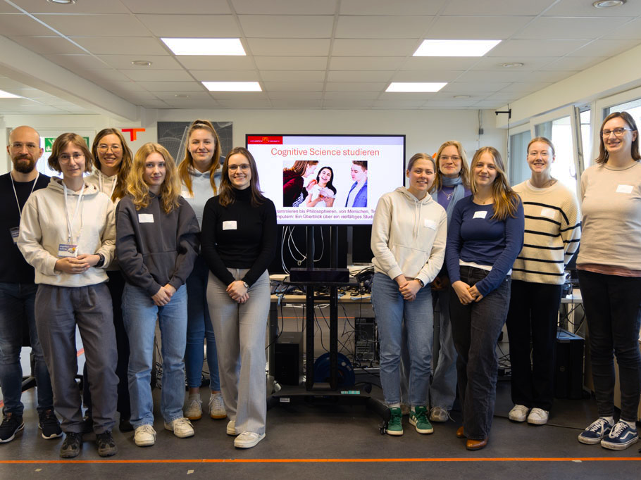 Mehrere junge Frauen und ein Mann stehen nebeneinander vor einem Computerbildschirm mit Präsentation und lächeln in die Kamera