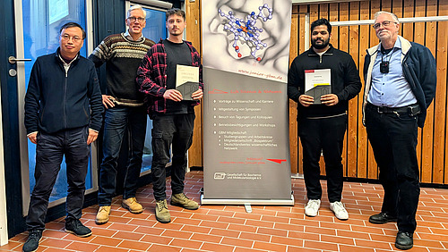 F&uuml;nf Personen l&auml;cheln in die Kamera. Die zwei in der Mitte stehenden halten Urkunden in den H&auml;nden.