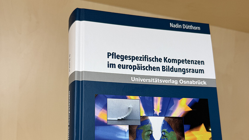 Ein Fachbuch von Nadin D&uuml;tthorn mit dem Titel "Pflegespezifische Kompetenzen im europ&auml;ischen Bildungsraum" steht in einem Regal.