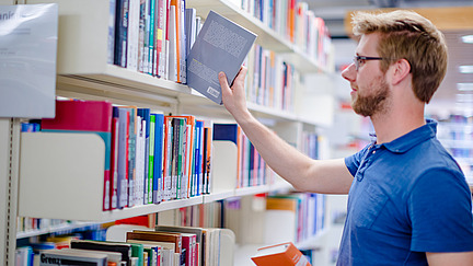 A man in the Alte Münze library pulls a book from a bookshelf.