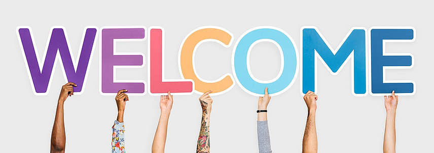 Hands hold up colourful letters that spell out the word ‘Welcome’.