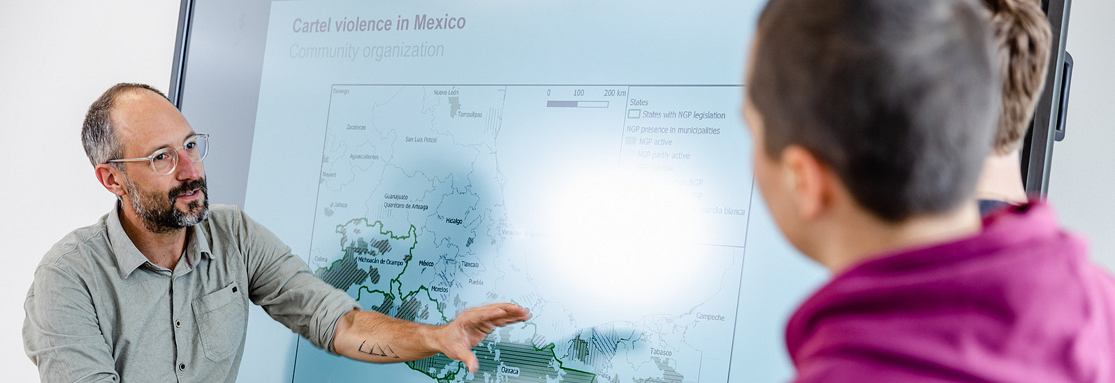 Teacher stands with two students at a whiteboard and explains a diagram