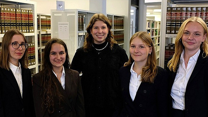 Fünf junge Frauen in förmlicher Kleidung in einer Reihe mit Bibliothek im Hintergrund