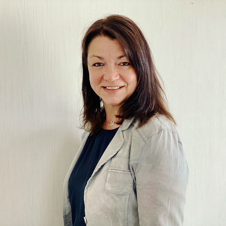 Frau mit dunklen halblangen Haaren schaut freundlich in die Kamera