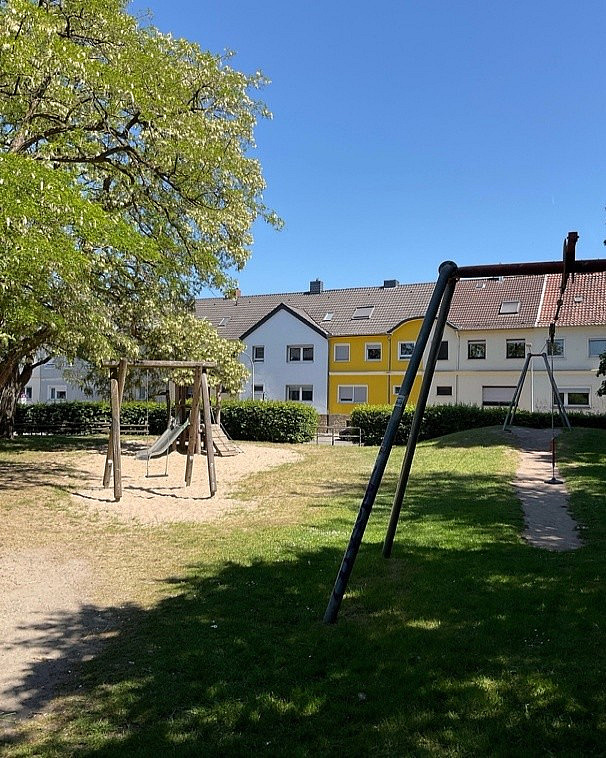 Spielplatz mit Rutsche, Schaukel und Seilbahn mit H&auml;usern im Hintergrund