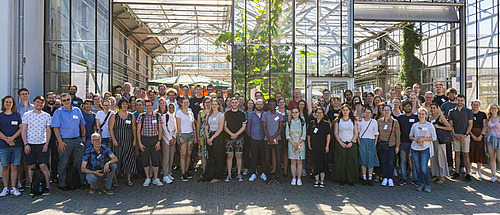 Eine gro&szlig;e Gruppe von Menschen steht vor einem Gew&auml;chshaus