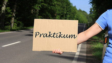 Eine Person trampt mit Pappschild - auf dem Schild steht "Praktikum"; A person is hitchhiking with a cardboard sign that says "Internship."