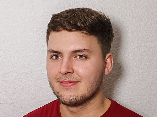 A man with brown hair wearing a red T-shirt smiles at the camera.