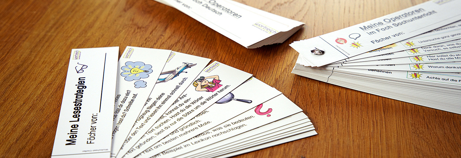 Verschiedene Papierfächer liegen auf dem Tisch. Man erkennt Fächer zur Lesestrategie und Operatoren im Sachunterricht. Die Fächer können personalisiert werden.