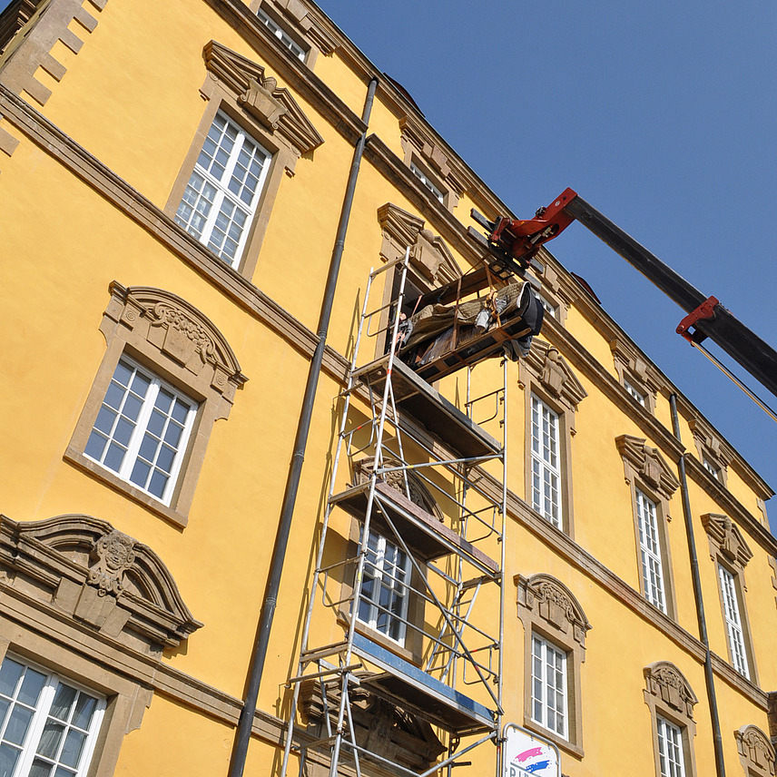 Blick von unten auf einen Kran, ein Musikflügel schwebt direkt vor einem geöffneten Fenster im zweiten Stock des Osnabrücker Schlosses.