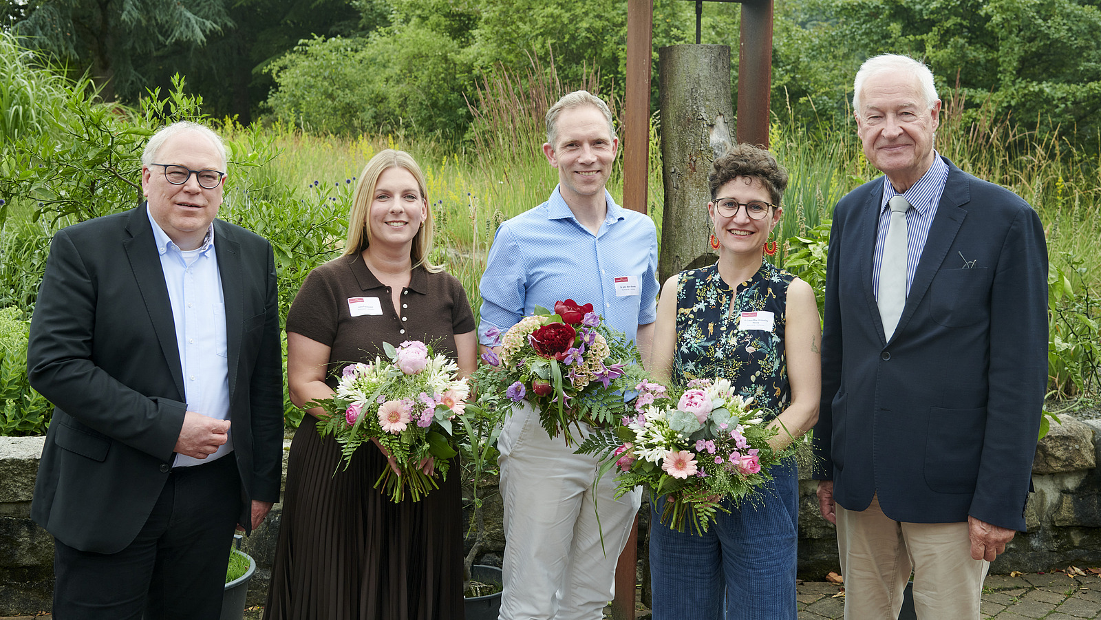 Mehrere Personen lächeln in die Kamera, die Personen in der Mitte halten Blumensträuße