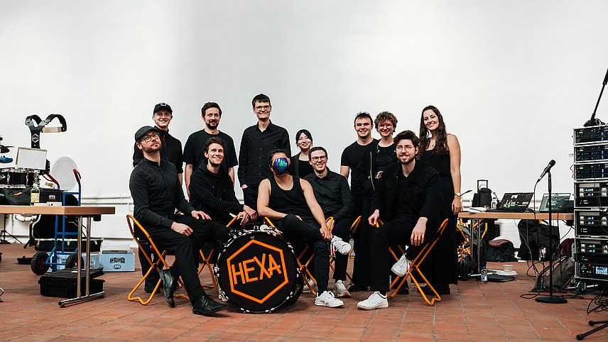 Gruppenfoto einer Band aus jungen M&auml;nnern und Frauen zwischen Instrumenten