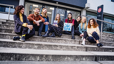 The picture shows young people sitting on a staircase in front of a building.