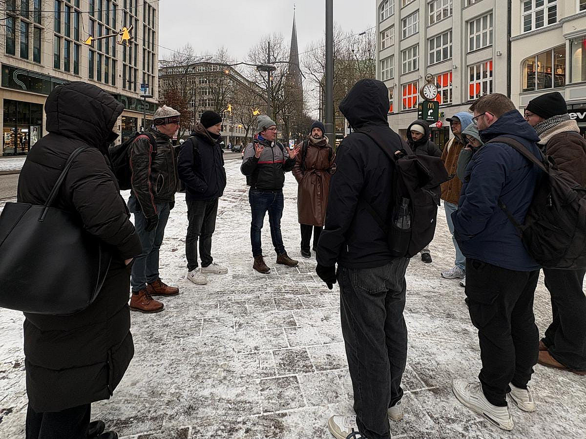 Das Bild zeigt eine Gruppe Menschen in Winterjacken in einer leicht verschneiten Fu&szlig;g&auml;ngerzone.