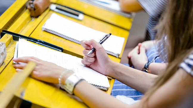 Students sit in a lecture hall. Sheets lie in front of them.