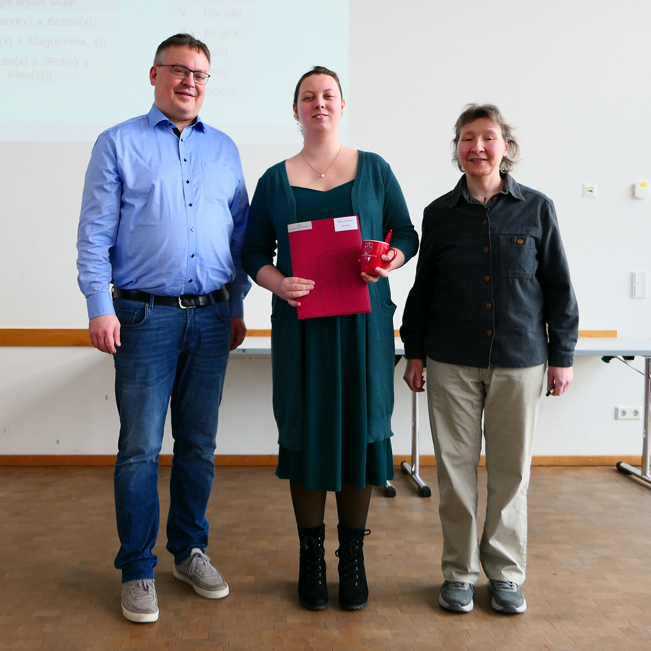 Eine Studentin steht mit ihrem Abschlusszeugnis zwischen Dekan und Studiendekanin.