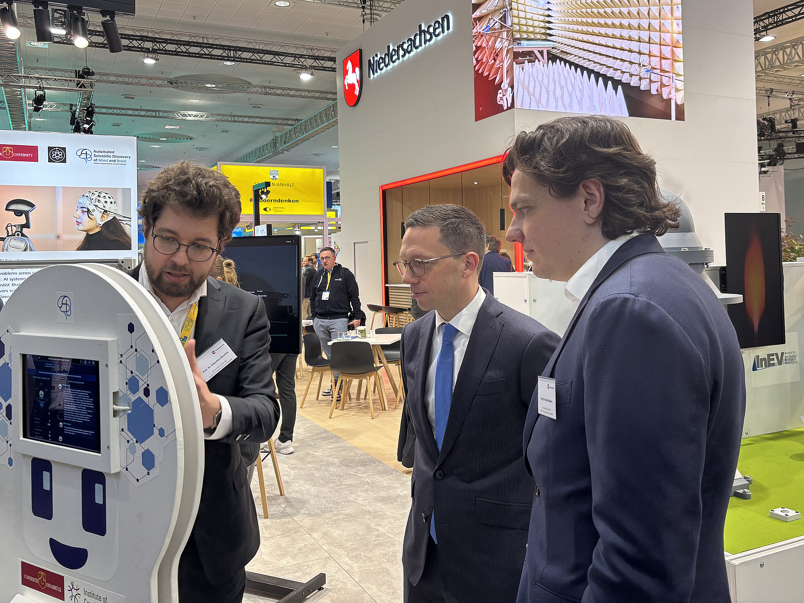 Drei M&auml;nner stehen nebeneinander und betrachten einen Bildschirm.