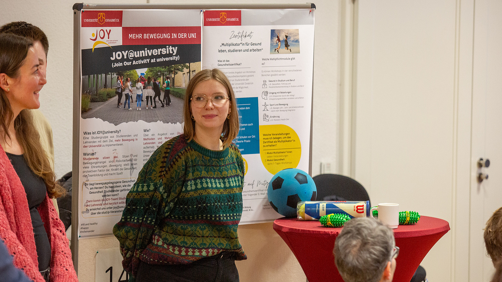 Mehrere weibliche Personen vor einer Stellwand, daneben Tisch mit Sportgeräten