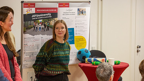 Mehrere weibliche Personen vor einer Stellwand, daneben Tisch mit Sportgeräten