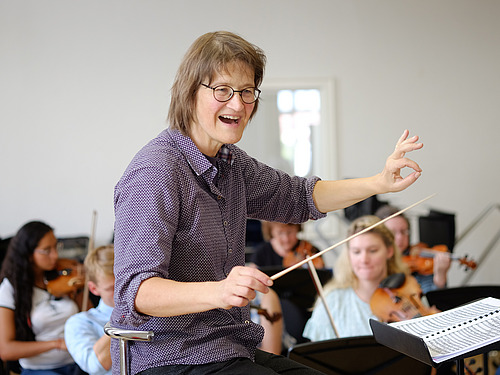 A woman passionately conducts an orchestra.