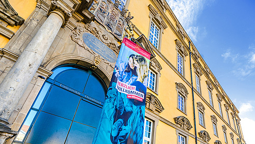 Eine Werbefahne mit dem Slogan "Sch&ouml;n dass ihr da seid" vor dem Eingang des Schlosses.