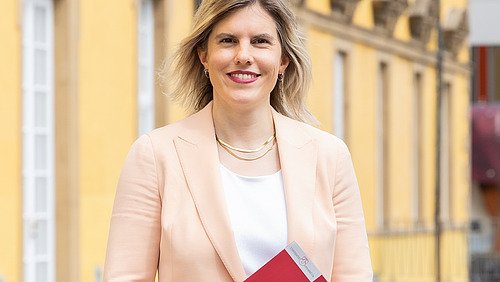 A woman stands in front of a castle with a folder in her hands.