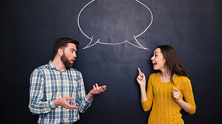 Zwei Menschen unterhalten sich vor einer Schultafel; Two people are having a conversation in front of a chalkboard.