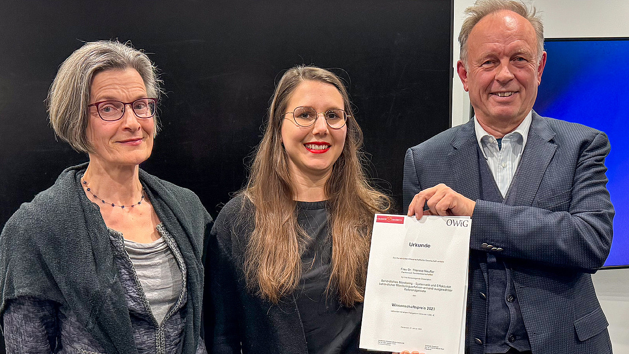 Zwei Frauen und ein Mann l&auml;cheln in die Kamera, der Mann h&auml;lt eine Urkunde in der Hand