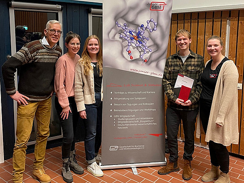Five smiling persons, the second from the right is holding documents