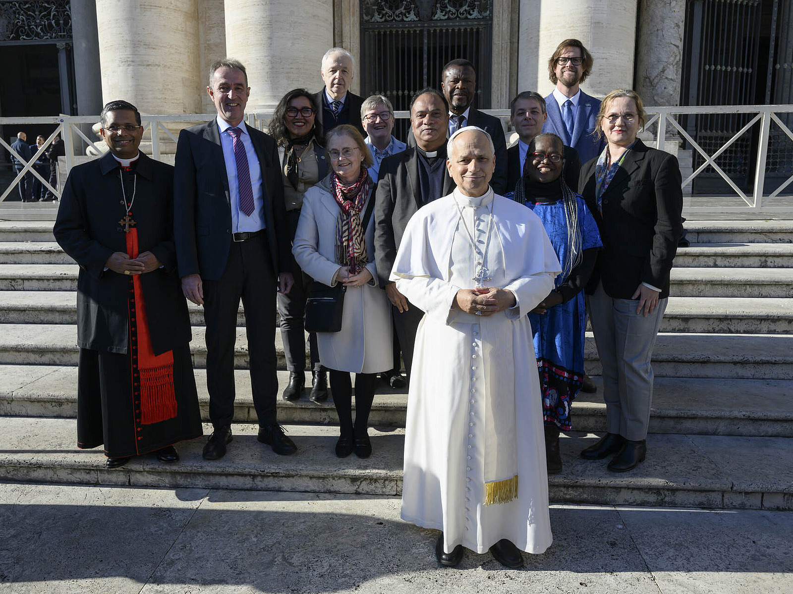 Papst Leo XIV. steht einige Schritte vor dem Komitee. Die Gruppe steht auf einer Au&szlig;entreppe und schaut in die Kamera.