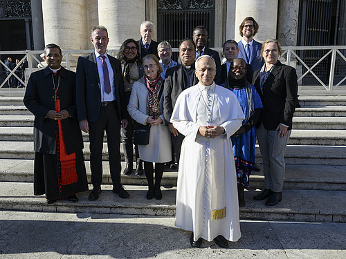 Papst Leo XIV. steht einige Schritte vor dem Komitee. Die Gruppe steht auf einer Au&szlig;entreppe und schaut in die Kamera.