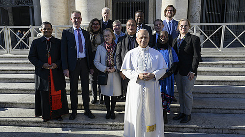 Papst Leo XIV. steht einige Schritte vor dem Komitee. Die Gruppe steht auf einer Au&szlig;entreppe und schaut in die Kamera.