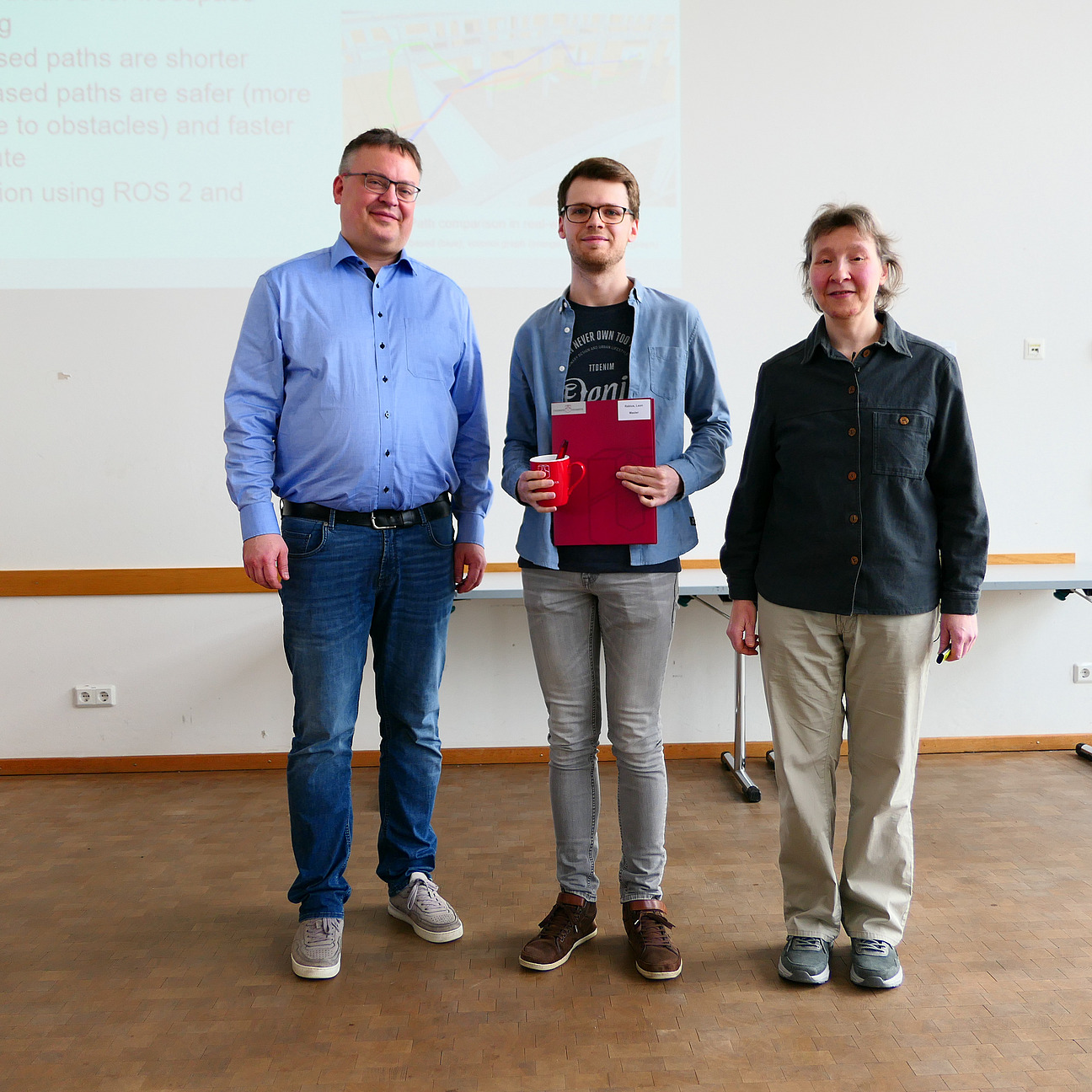 Ein Student steht mit seinem Abschlusszeugnis zwischen Dekan und Studiendekanin.