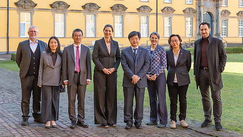 A group of people in trouser suits stand next to each other in the courtyard of a castle and smile at the camera
