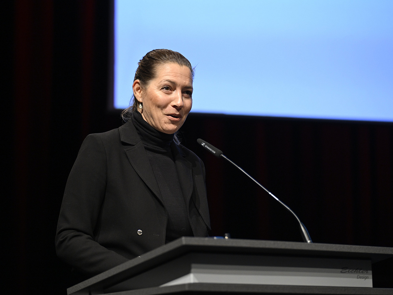 University President Prof. Dr. Susanne Menzel-Riedl stands at the microphone. 