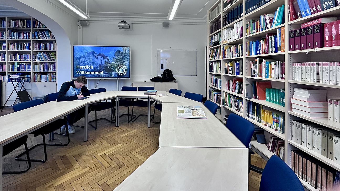 Die Mediothek mit einer gro&szlig;en Besprechungsrunde und einem B&uuml;cherregal nebenan