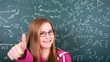 Girl sitting in front of a blackboard with mathematical formulae