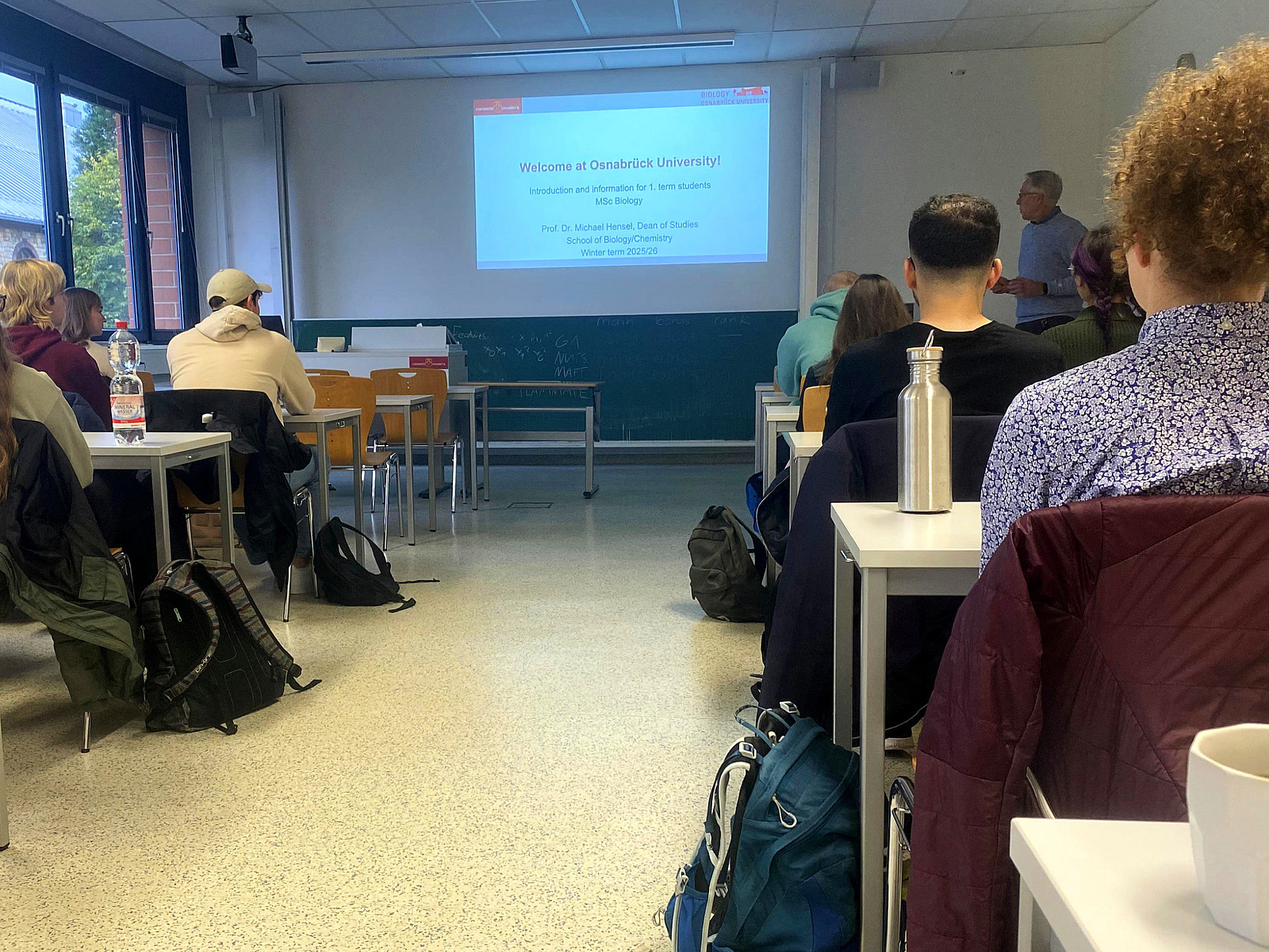 Students are sitting in a seminar room, and at the front there is a presentation with the words ‘Welcome to Osnabrück University’.