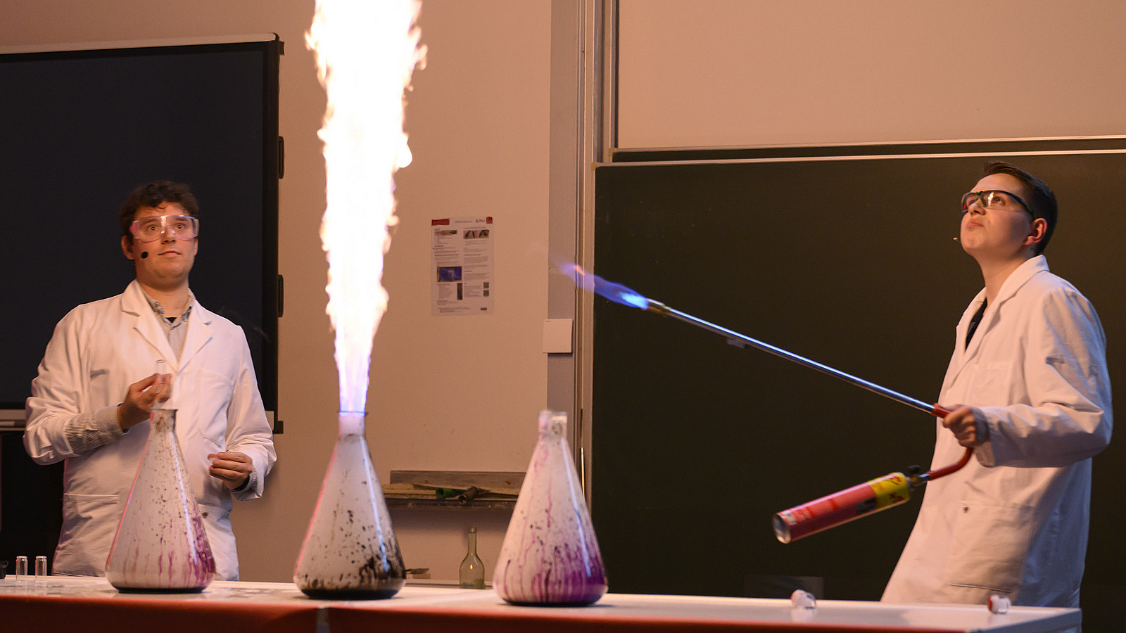 Personen in wei&szlig;en Kitteln unternehmen chemische Experimente, dabei entsteht Flamme