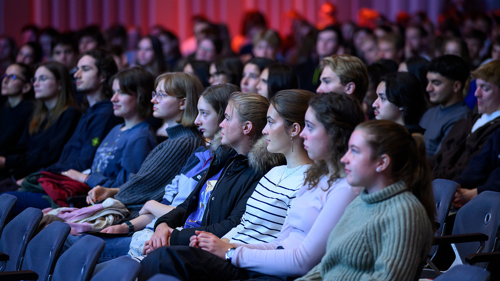 Close-up of packed rows of spectators in a hall. The people are looking intently toward the stage.
