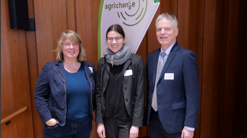 Drei Personen stehen vor einer Beachflag und l&auml;cheln in die Kamera