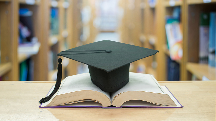 Graduation cap over open books in a library room.
